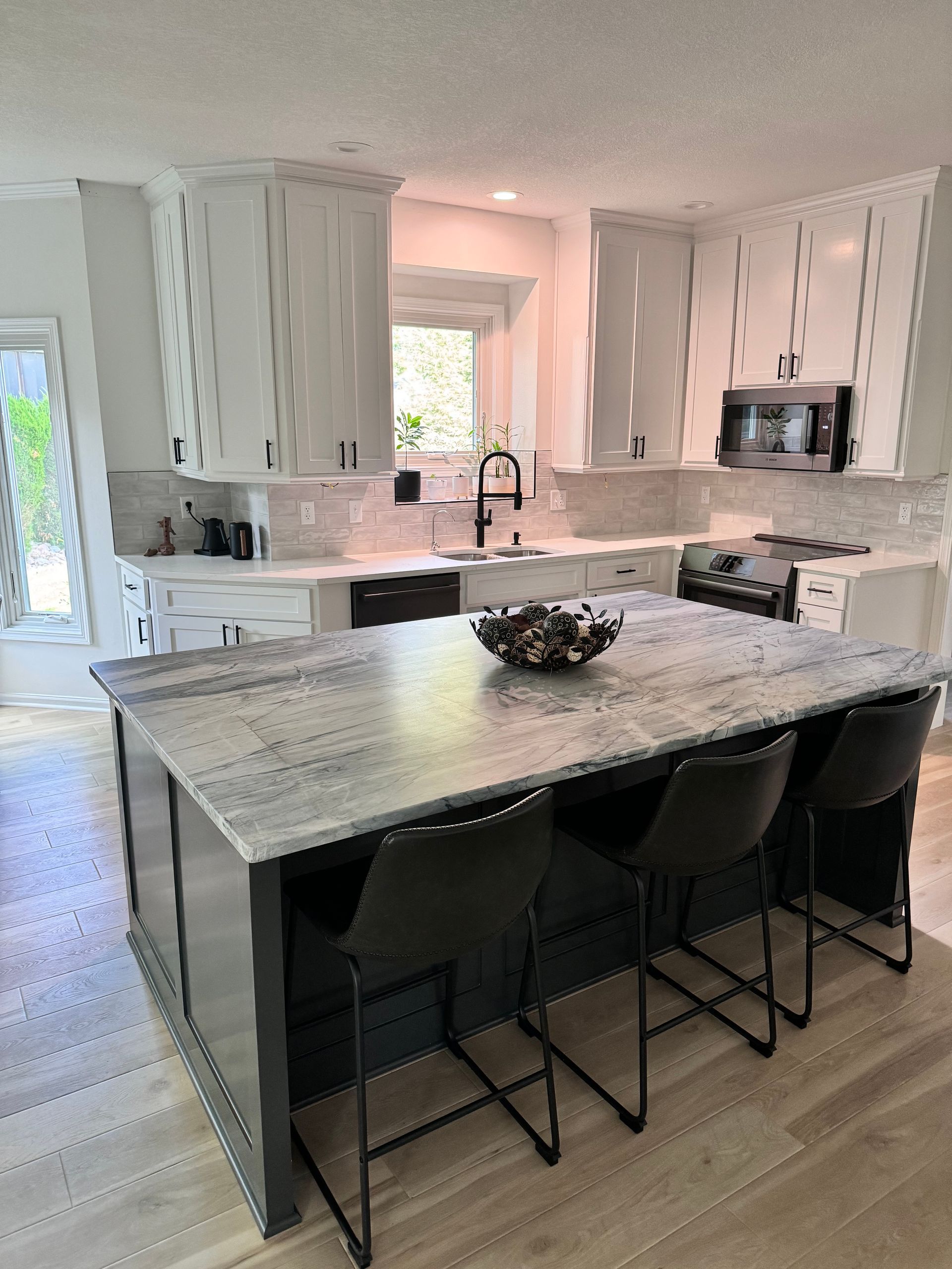 A modern kitchen featuring a dark blue island with marble countertop, white cabinetry, stainless appliances, and stools.