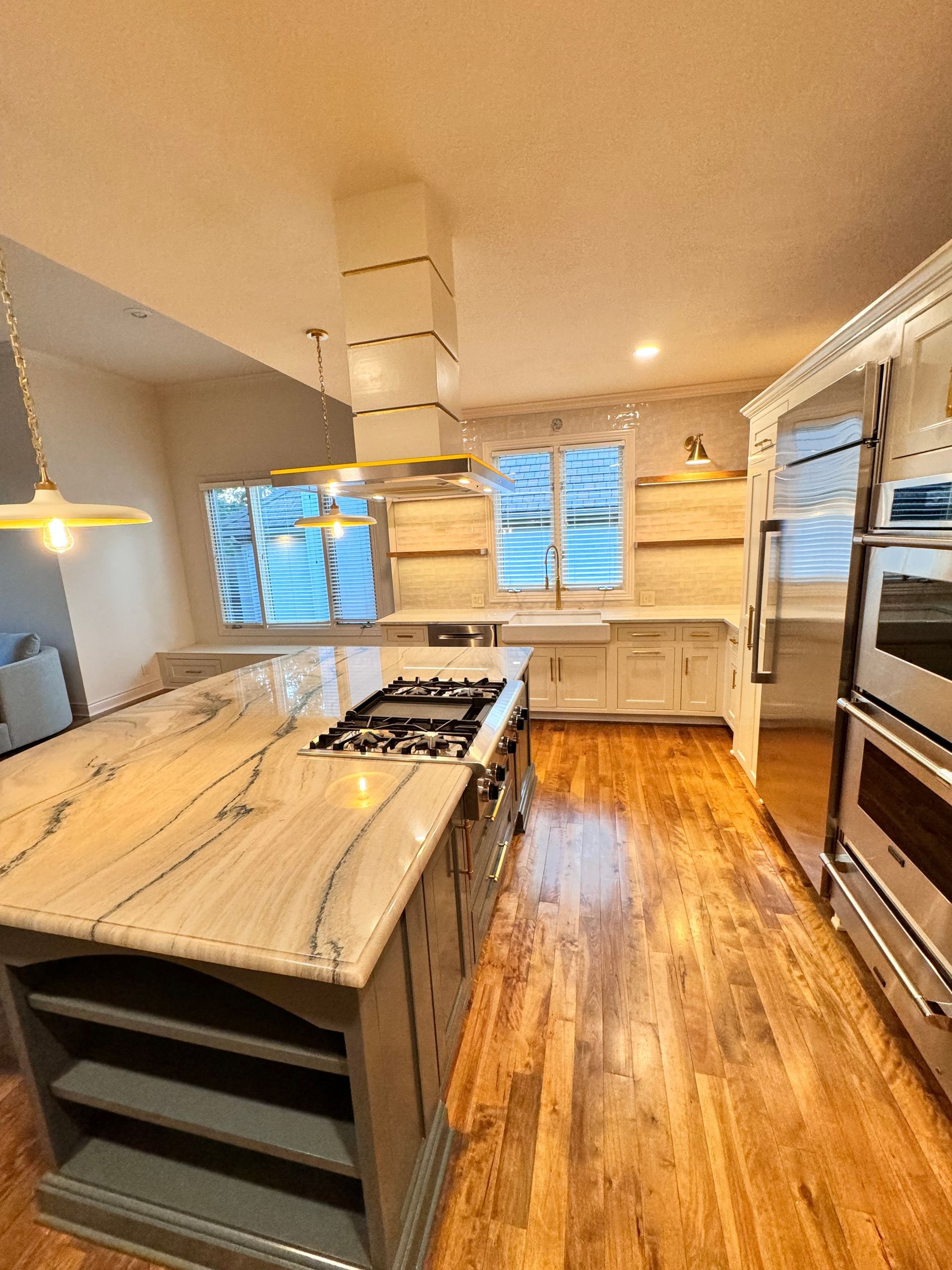 A modern kitchen features a large island with stone countertops, white cabinetry, open shelving, and light wood flooring.
