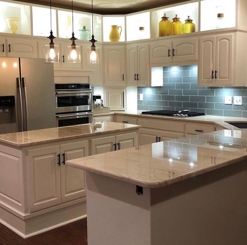 A bright kitchen with white cabinets, beige granite countertops, stainless steel appliances, and a gray tiled backsplash.