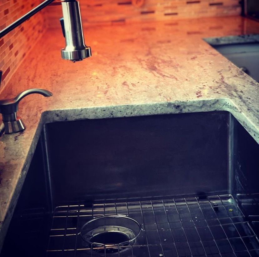 A stainless steel kitchen sink with a metal grate at the bottom, a faucet, and a soap dispenser against a tiled backsplash.