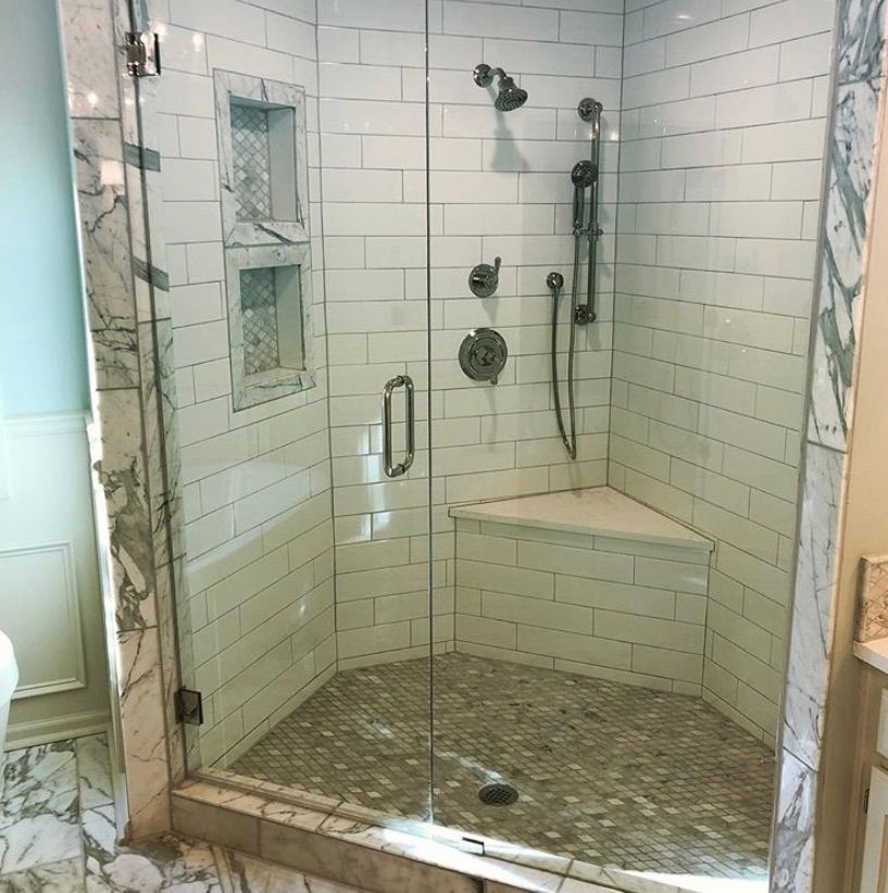 A walk-in shower with white subway tile walls, a marble-tiled floor, a corner bench, and two wall niches.
