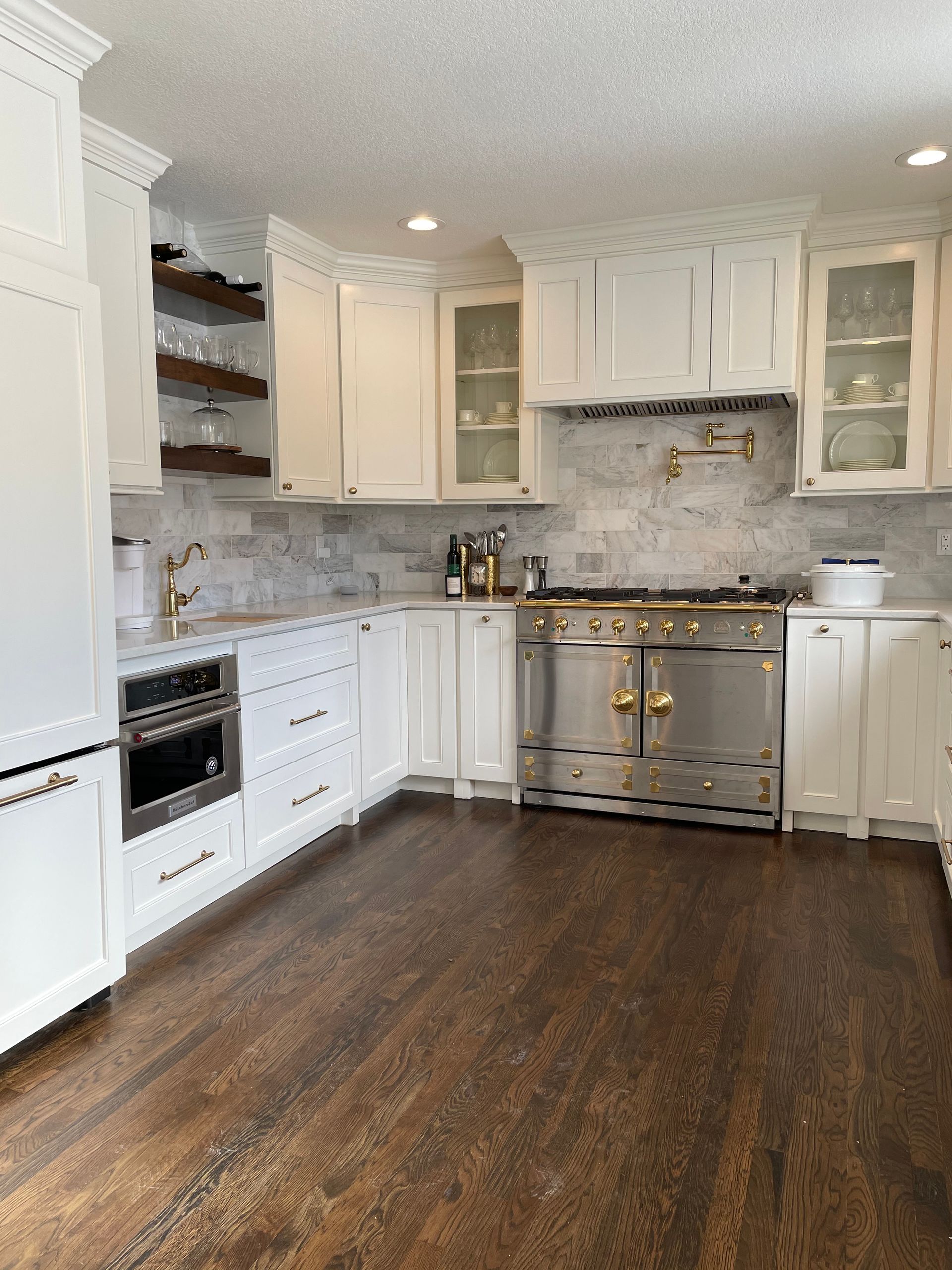 A bright kitchen with white cabinets, marble backsplash, dark wood flooring, and stainless steel professional-style range.