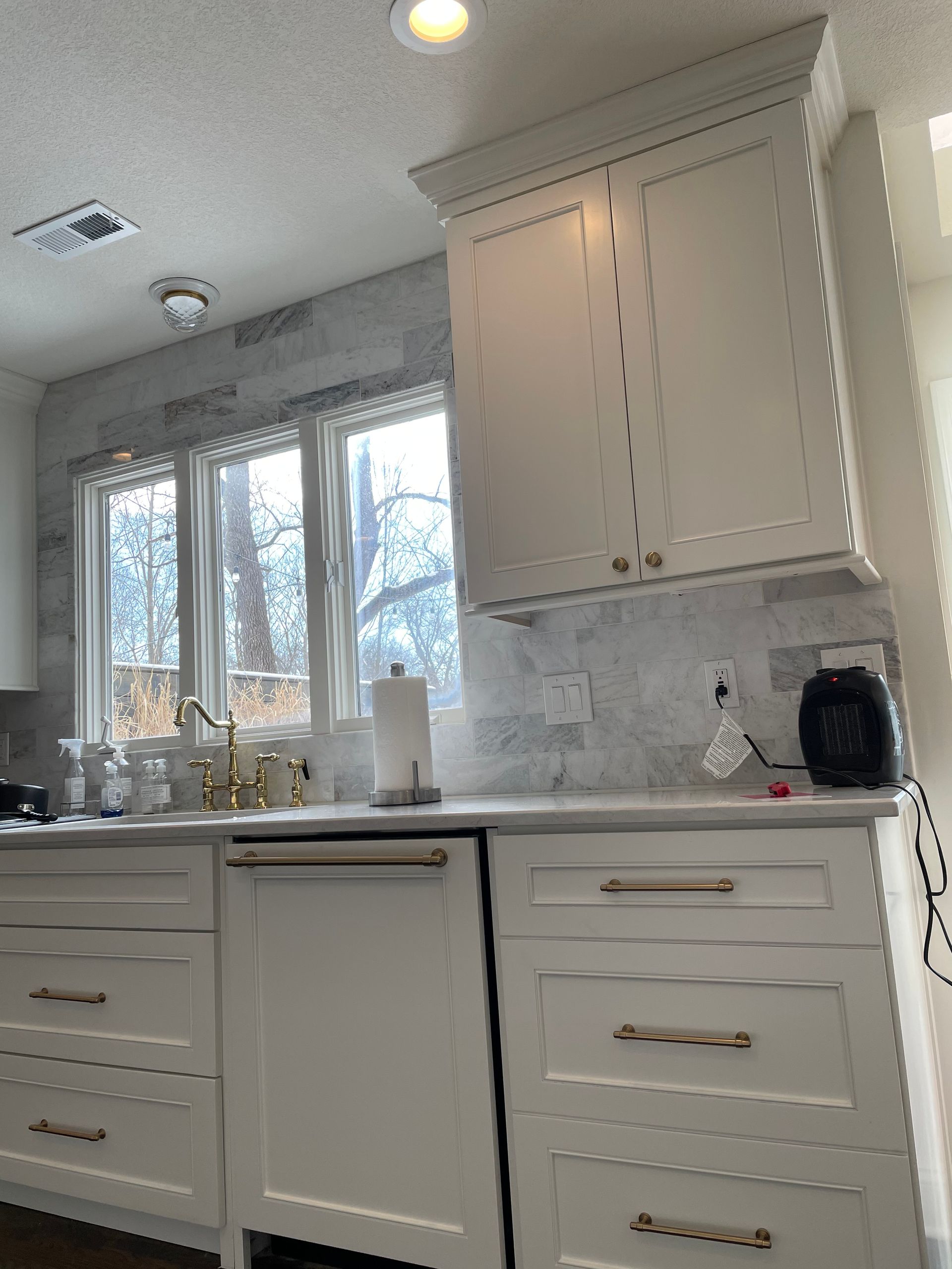 A modern kitchen featuring off-white shaker-style cabinets, brass hardware, and a marble tile backsplash above the counter.