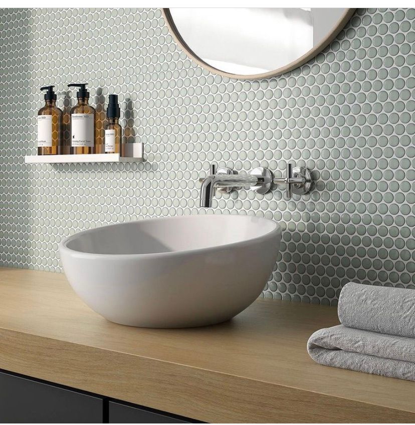 A modern bathroom vanity with a white vessel sink, wall-mounted faucet, and stacked towels against gray penny-tile walls.