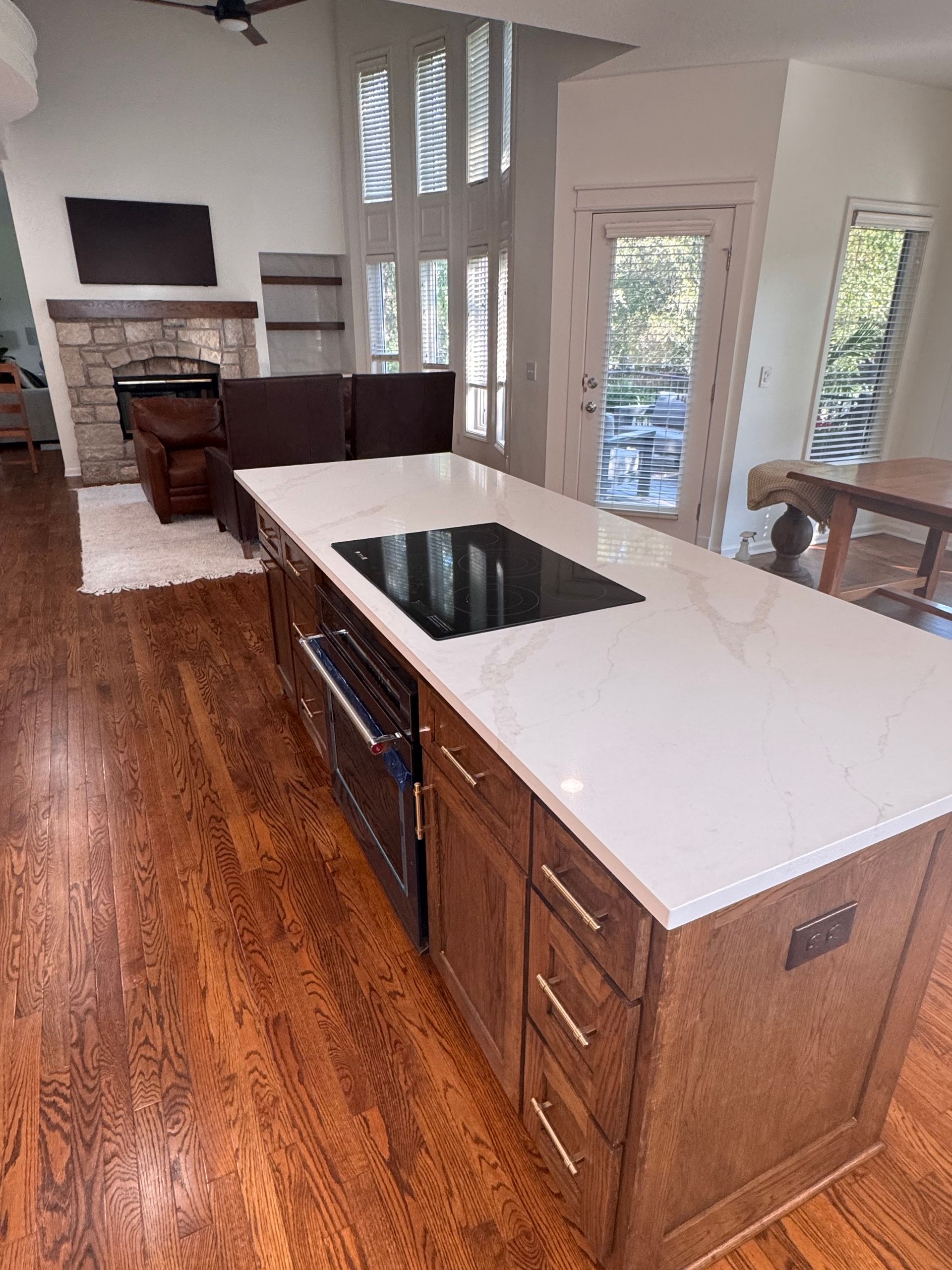 A modern kitchen island with a white countertop and black cooktop, centered in a room with hardwood floors and a fireplace.