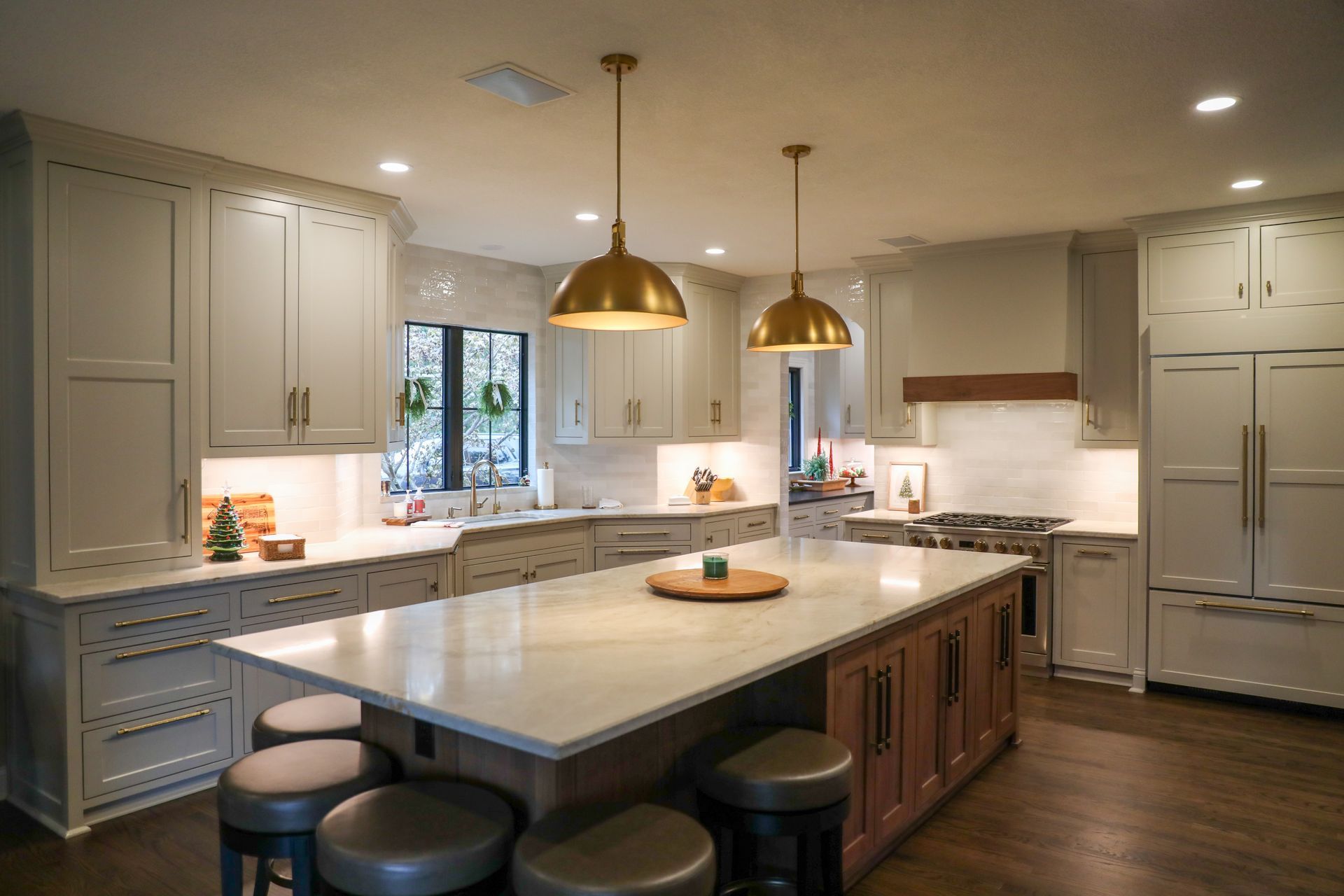 Modern kitchen with white cabinets, a large central island, bronze pendant lights, and brown wood flooring.
