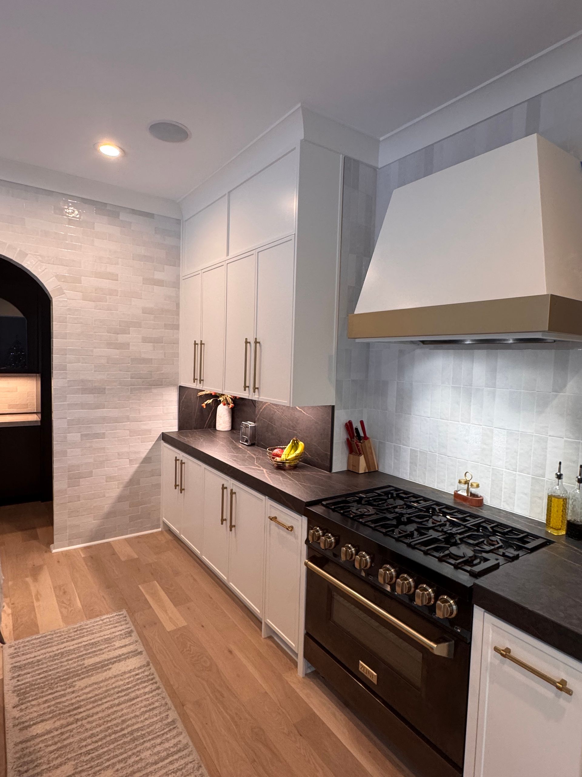 A modern kitchen with white cabinetry, dark countertops, a dark range, and a textured white backsplash.