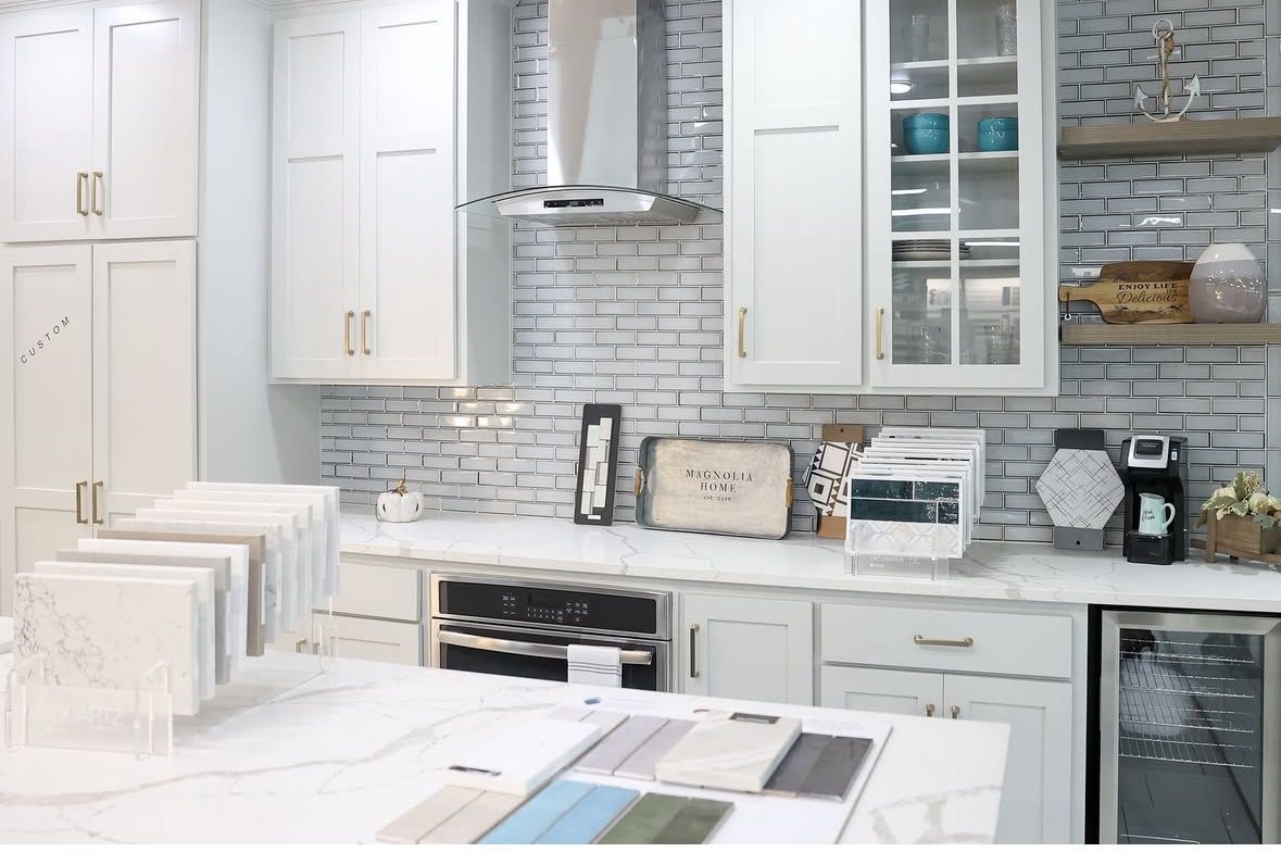 A showroom kitchen featuring white cabinets, a light stone countertop, subway tile backsplash, and material samples.