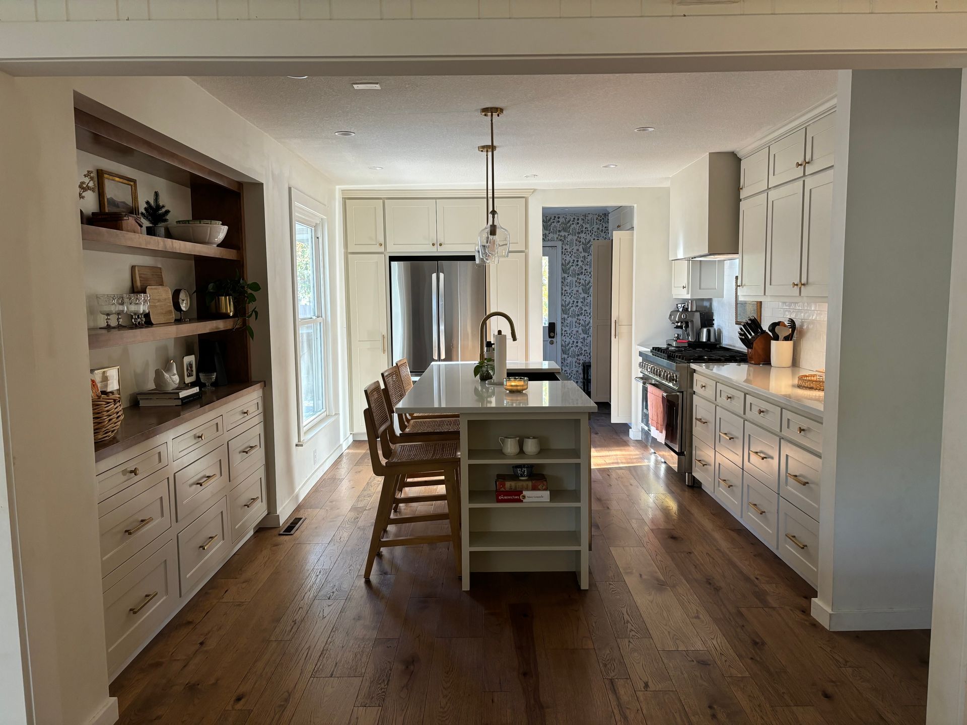 A bright, modern kitchen with white cabinets, wood flooring, an island with bar stools, and open wooden shelving.