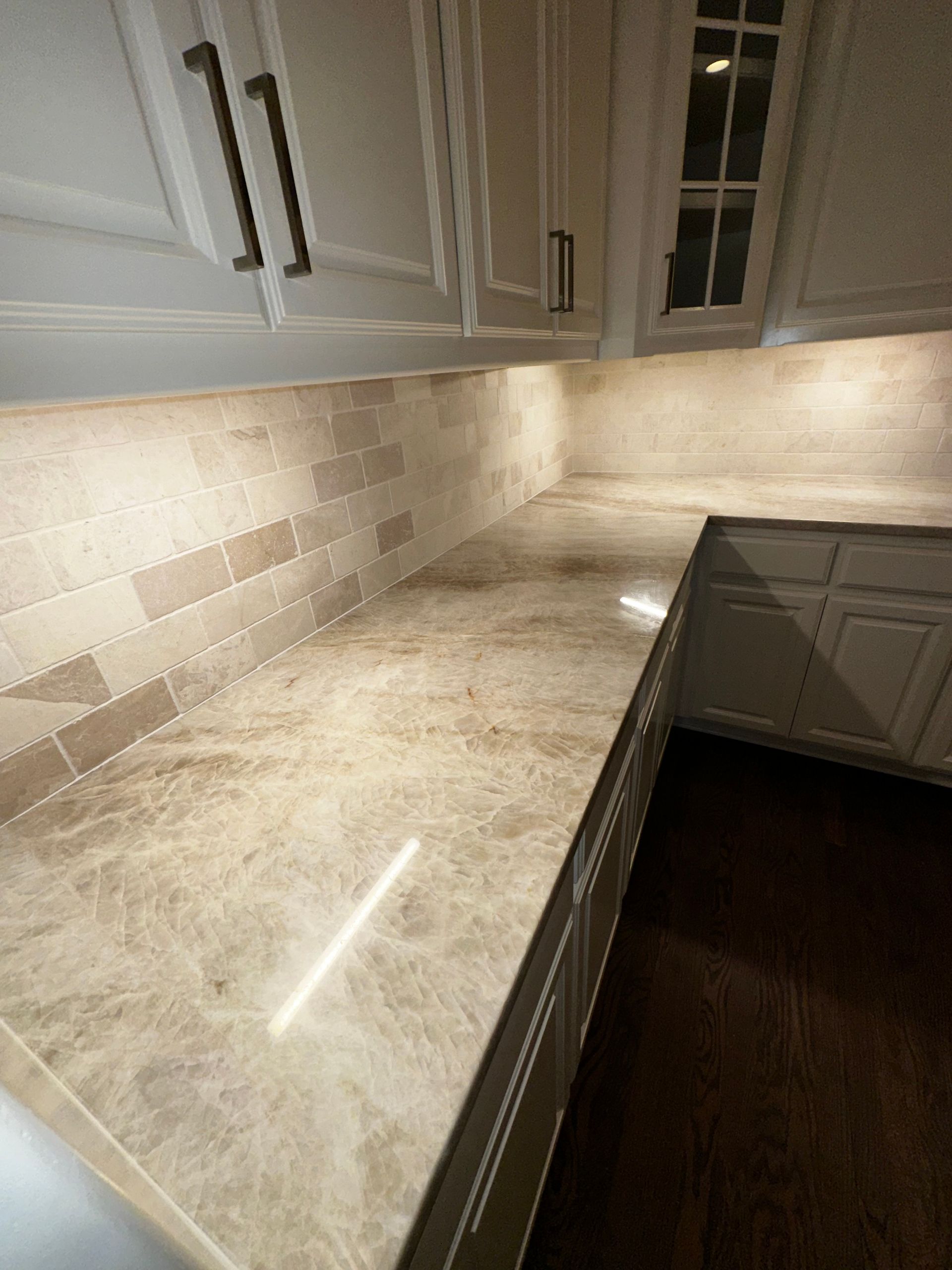 A kitchen counter with beige marble-patterned stone, a matching brick-style backsplash, and white cabinets.