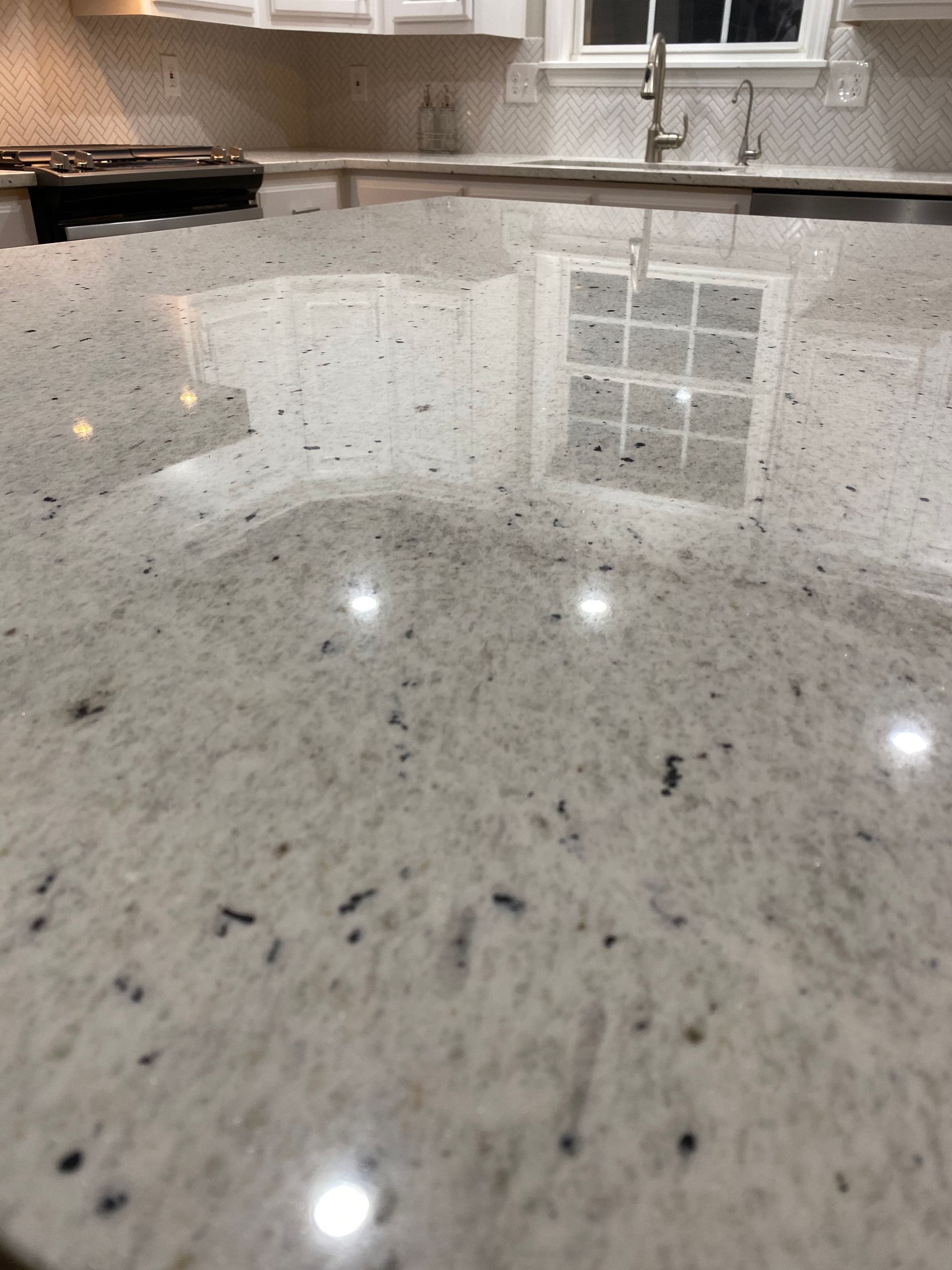 A minimalist white kitchen with marble countertops, a central island, and a coffered ceiling with inset lights.