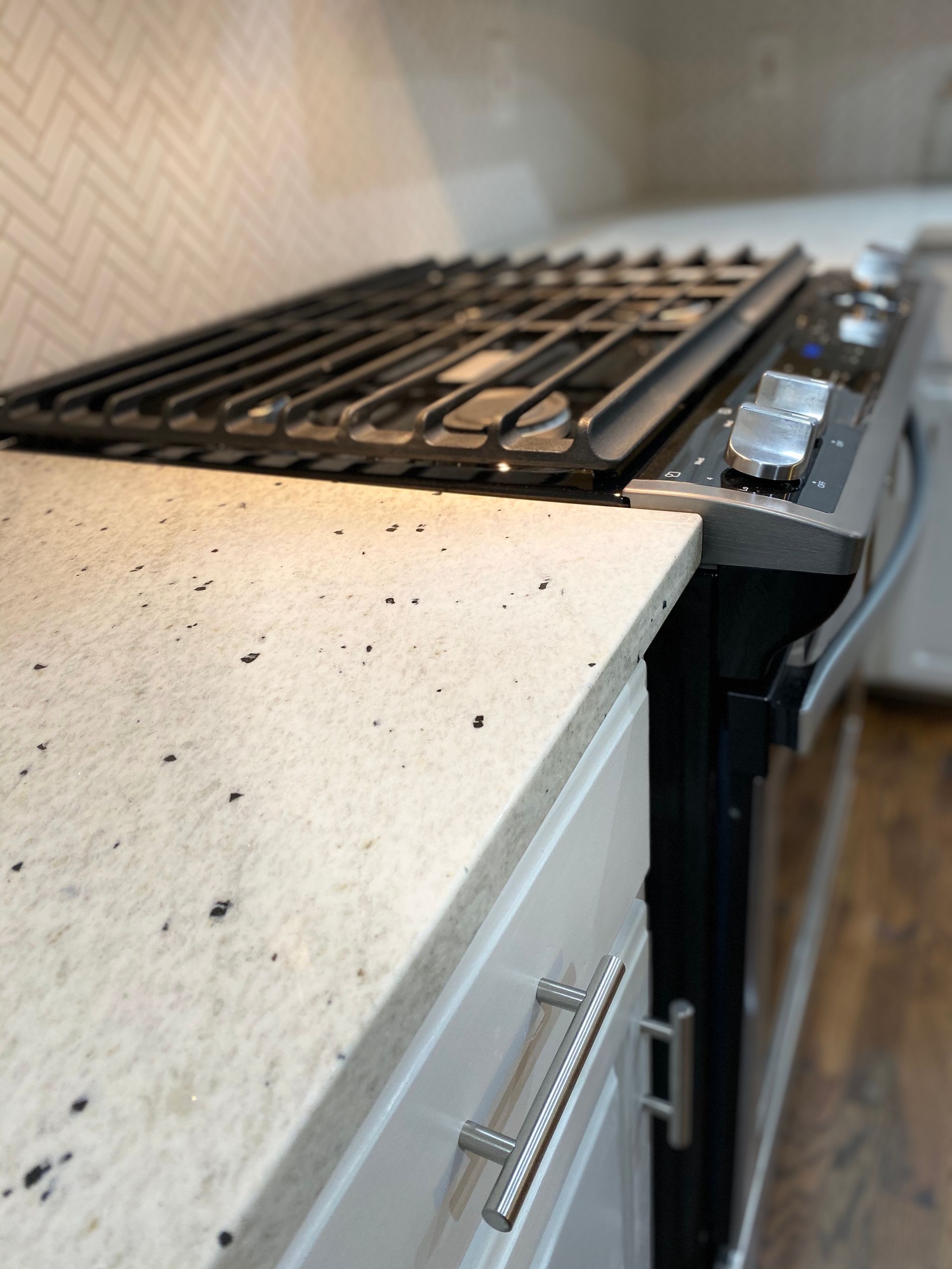 A high-angle view of a kitchen range next to light-colored, speckled countertops with white cabinets.
