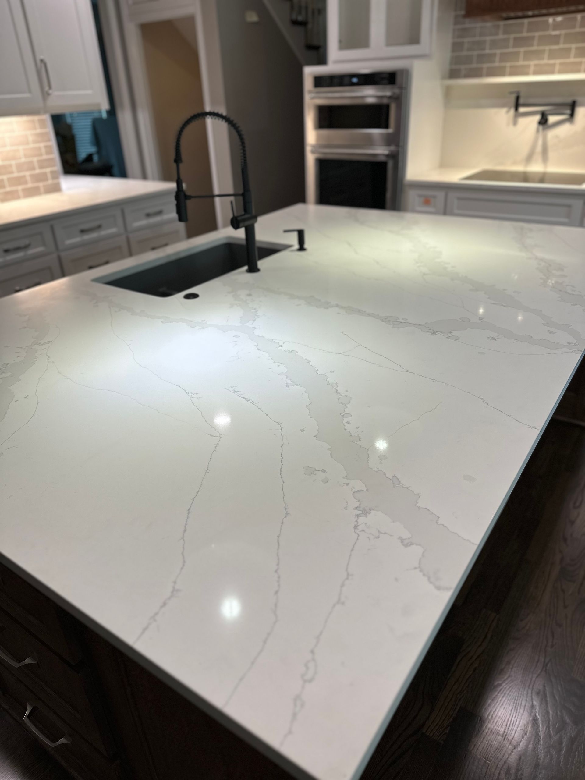A white marble-style kitchen island with a dark sink and faucet in a modern kitchen setting.