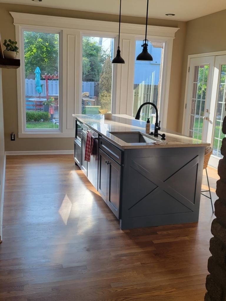 A modern kitchen island with dark blue cabinetry, an X-patterned side, and a sink, set on wooden floors before large windows.