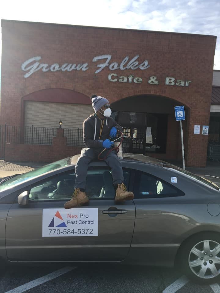 A man is sitting on the roof of a car in front of a grown folks cafe and bar.