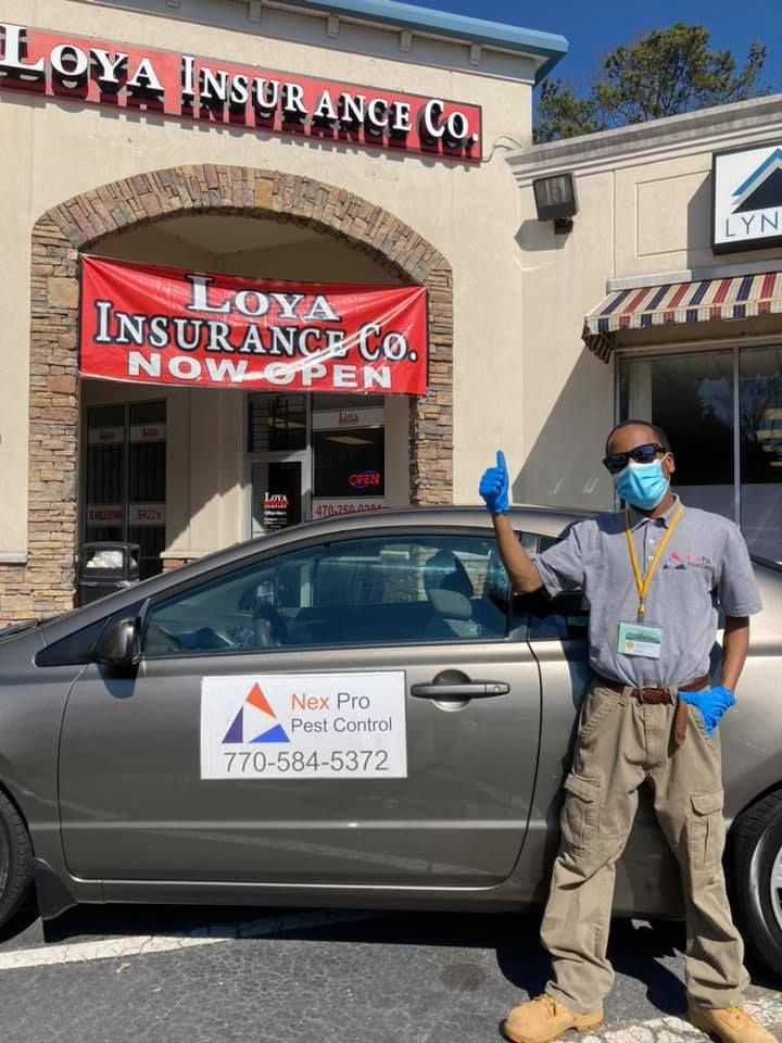 A man wearing a mask and gloves is standing next to a car in front of an insurance company.
