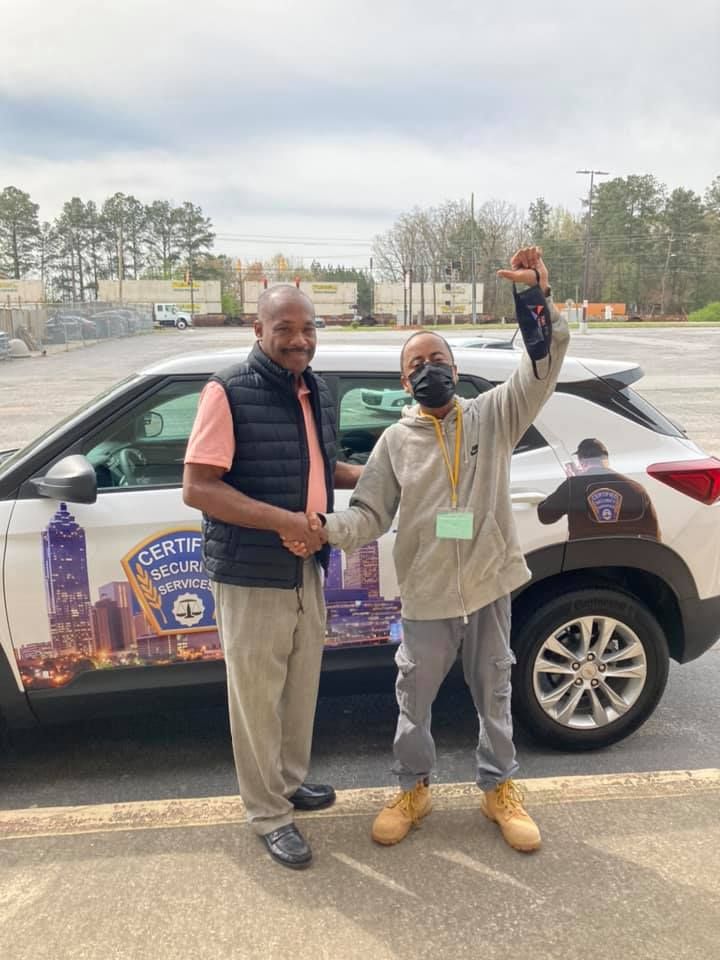 Two men are standing next to a car in a parking lot.