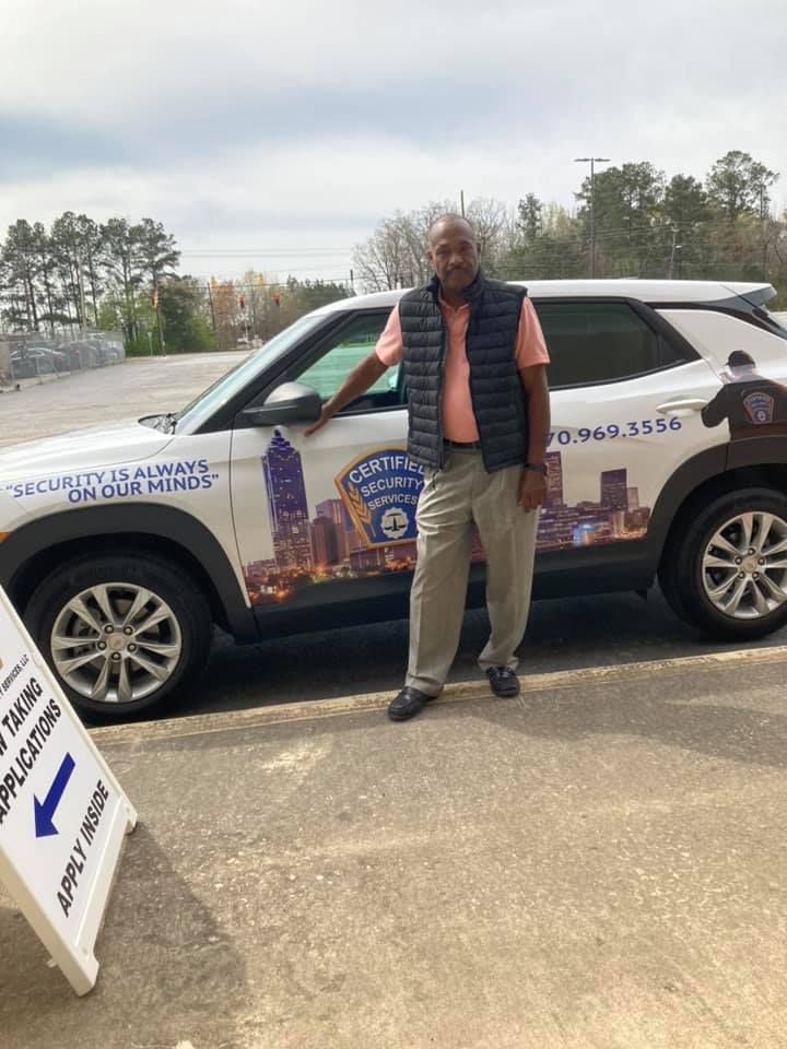 A man is standing in front of a car in a parking lot.