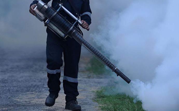 A man is using a machine to spray smoke on the grass.