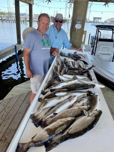 Two men are standing next to a table full of fish.
