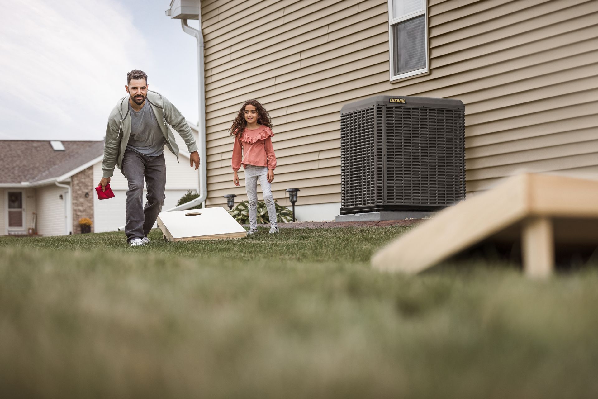 Two beige HVAC outdoor units sitting on a concrete pad against a brick wall next to a wooden fence.