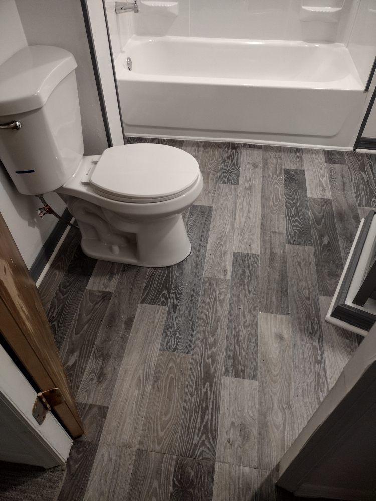 A bathroom with a white toilet next to a bathtub and grey wood-look flooring.
