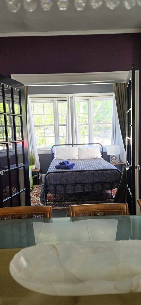 Bedroom with bed framed by windows, seen through open doors from another room.
