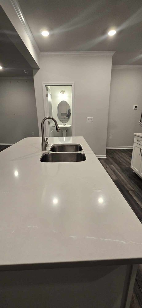 Kitchen island with double sink, faucet, and a view into a bathroom with an oval mirror.