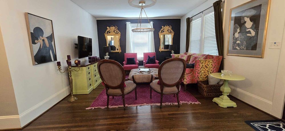 Living room with eclectic decor; dark purple wall, pink rug, vintage furniture.