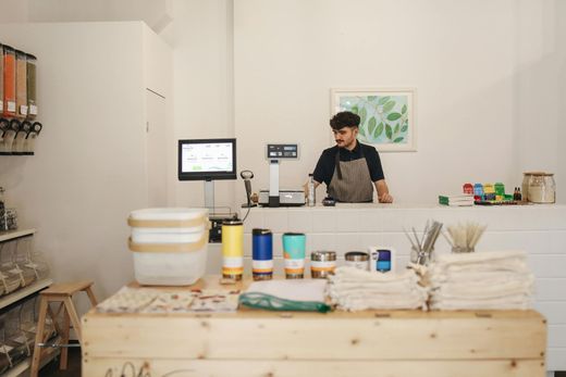 A shopkeeper behind a counter in a brightly lit store with scales and product displays.