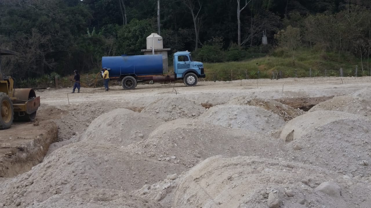 Sitio de construcción con montículos de arena, un camión de agua y trabajadores.