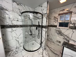 A bathroom with marble walls and a curved shower stall.