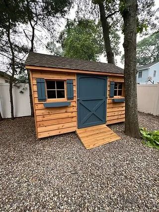 A wooden shed with a blue door and shutters in a gravel yard.