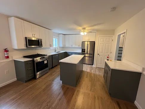 A kitchen with stainless steel appliances , white cabinets , hardwood floors and a large island.