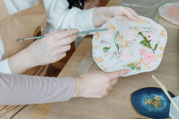 A person is holding a plate with flowers on it and pointing at it.