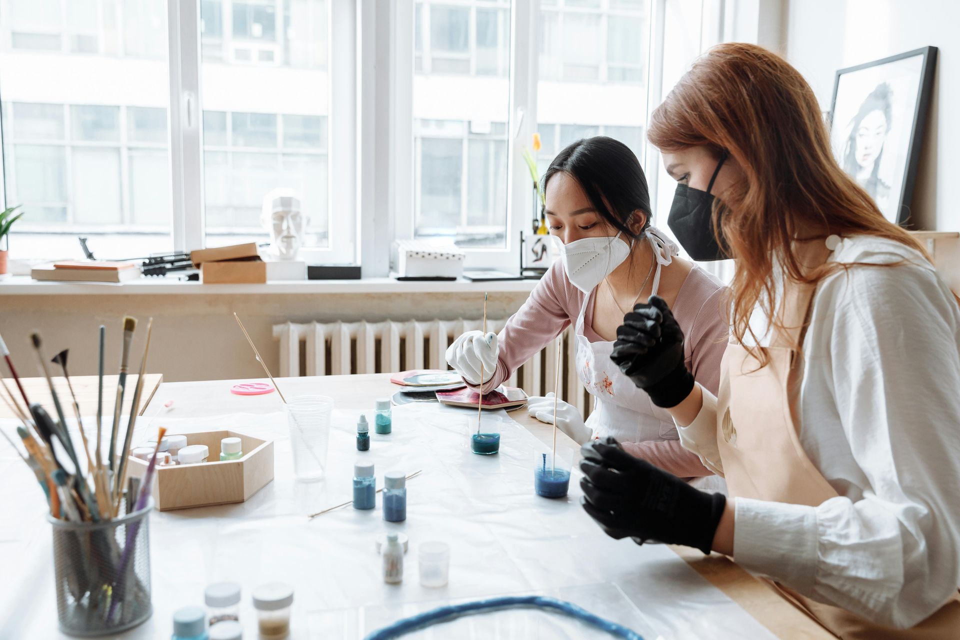 Two women wearing face masks are sitting at a table painting.