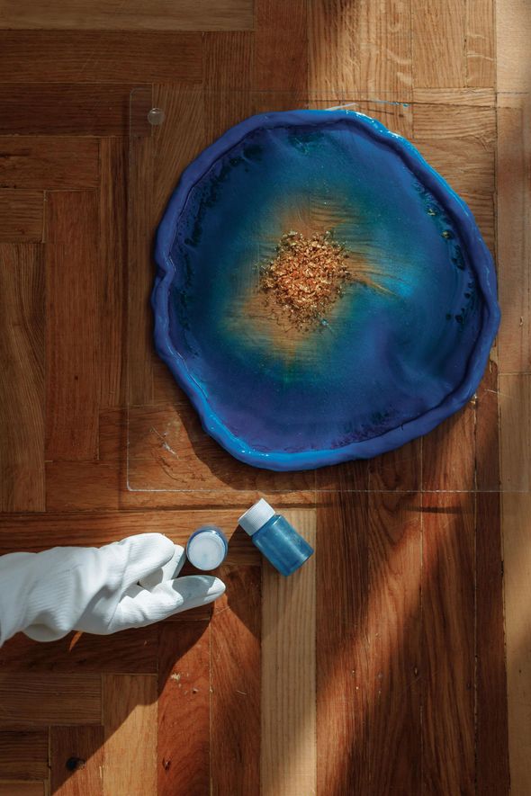 A person is painting a blue plate on a wooden table.