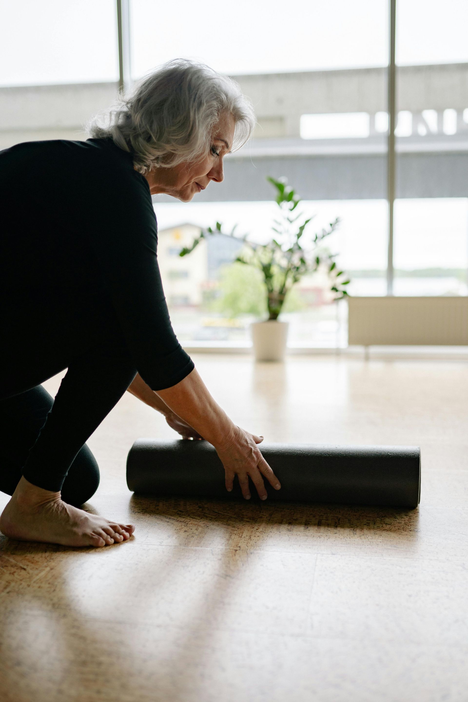 A woman is kneeling down on the floor rolling a yoga mat.