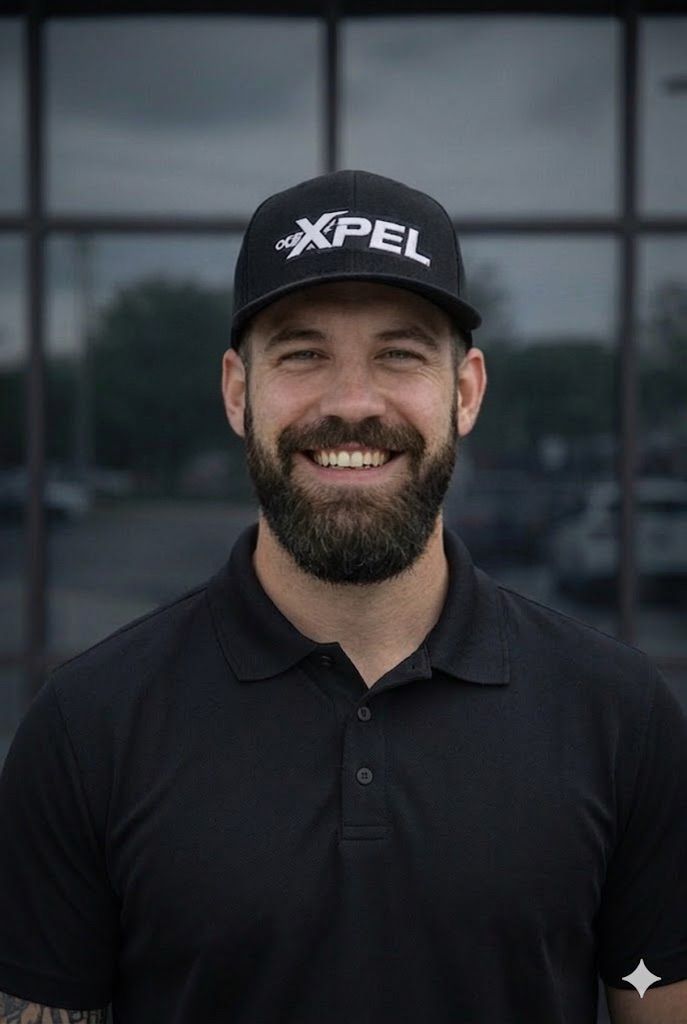 A smiling person with a beard, wearing a black polo shirt and a black 