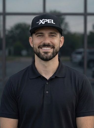 A smiling person wearing a black polo shirt and a black cap with an 