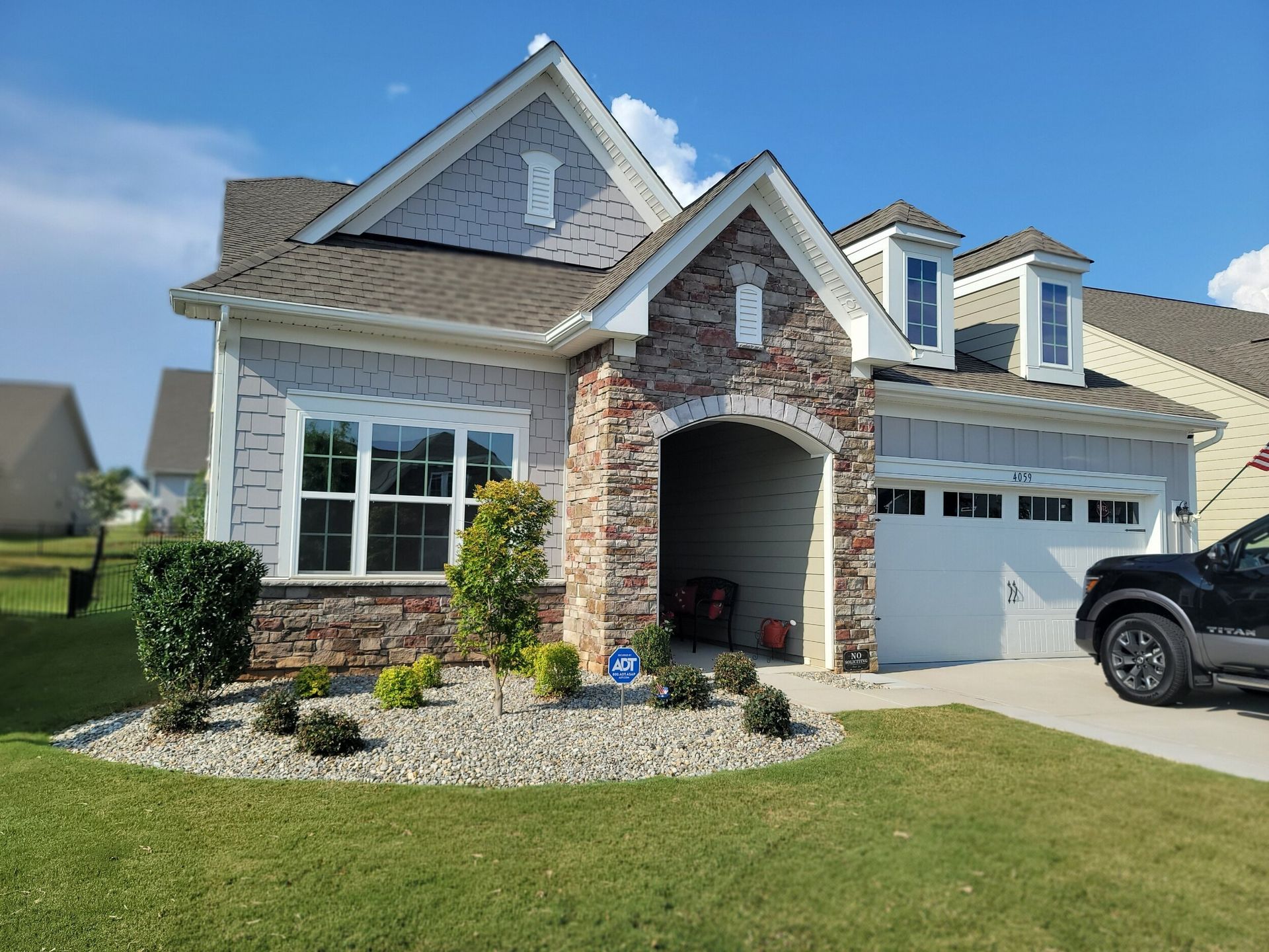 A two-story house with a brick and light-grey siding facade, a covered porch, and a white garage, under a blue sky.