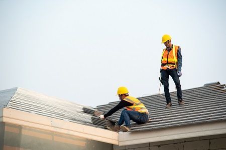 Two construction workers are working on the roof of a building.