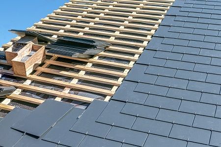 A roof is being built with slate tiles and wooden beams.