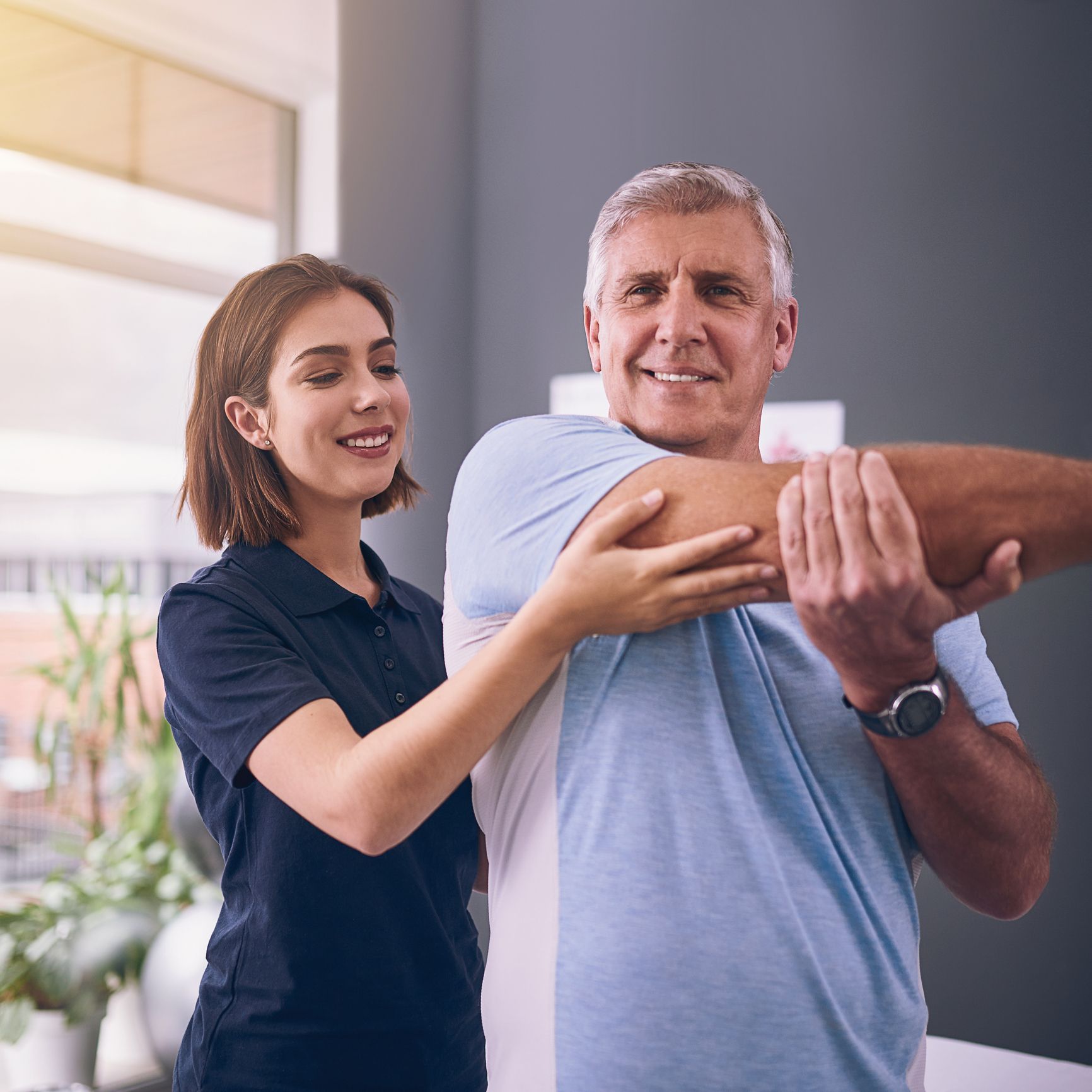 A woman is helping an older man stretch his arms - Mountain Home, AR - Long Chiropractic