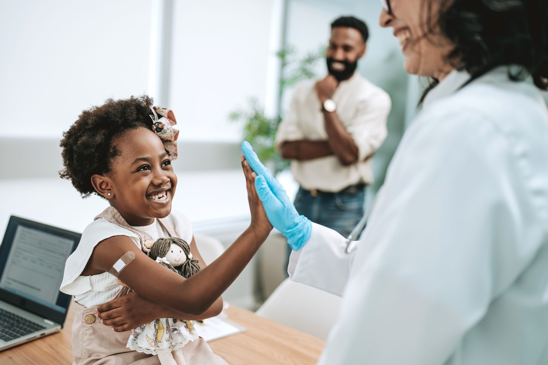 Happy child after being vaccinated giving a high-five to a doctor while father smiles in the background. Happy child after being vaccinated giving a high-five to a doctor while father smiles in the background.