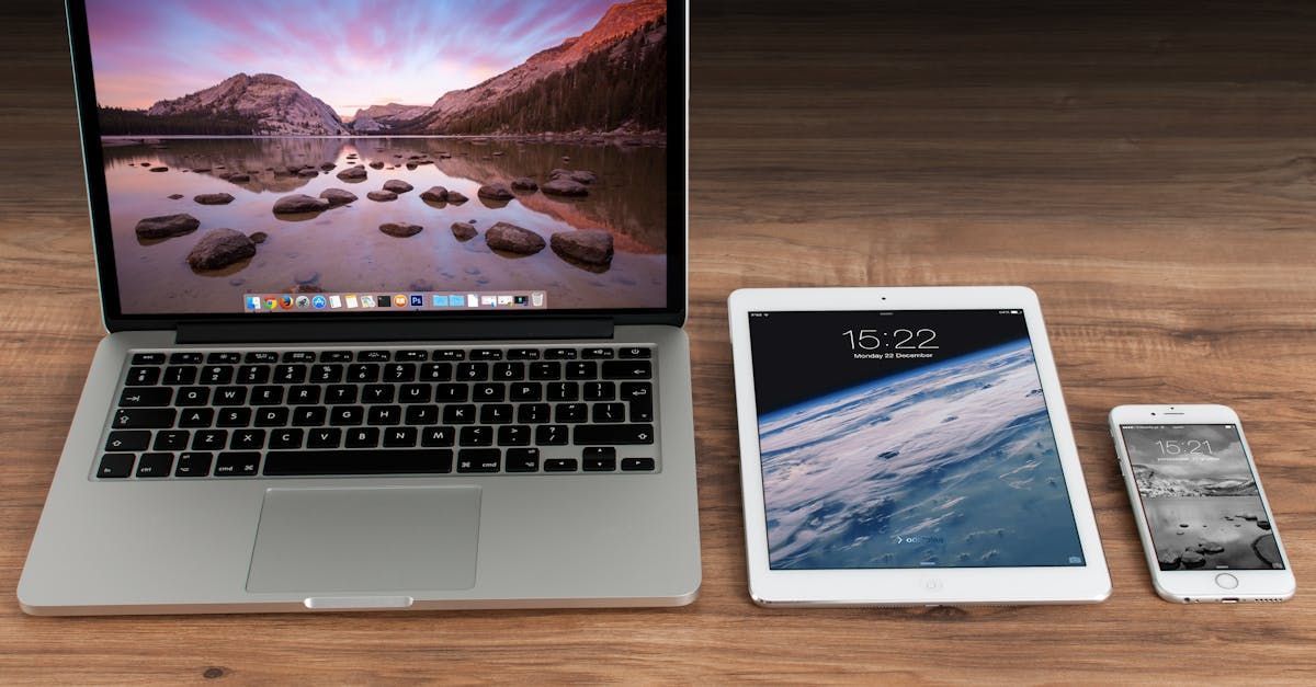 A laptop , tablet , and cell phone are sitting on a wooden table.