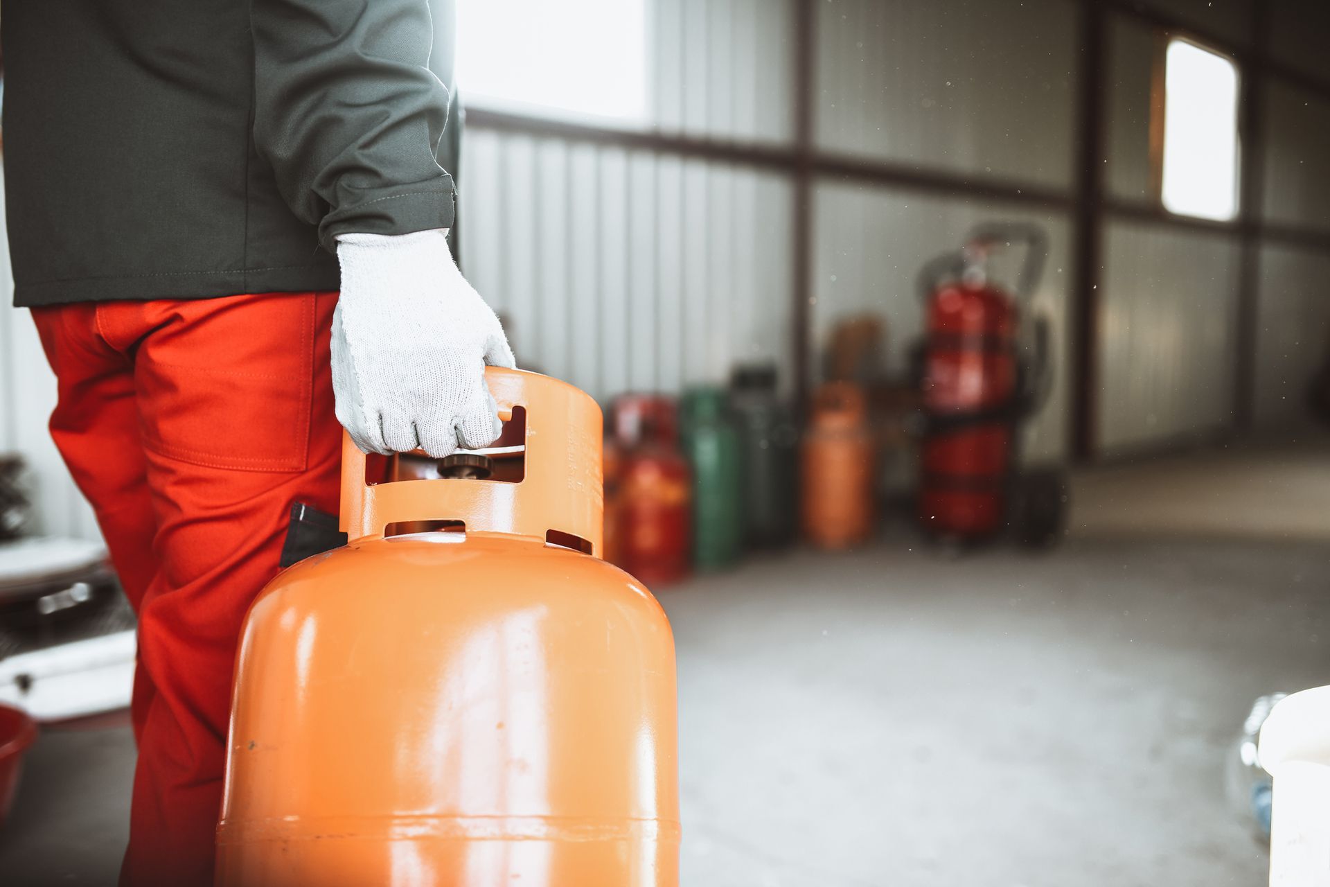 Worker handling orange propane tank in industrial gas storage area.