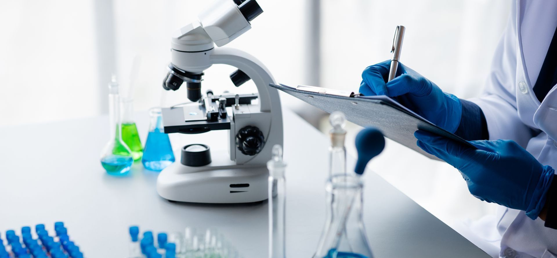a scientist is writing on a clipboard in a laboratory in front of a microscope .