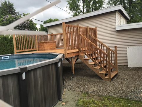 Piscine hors sol avec terrasse en bois et escalier à côté d'un bâtiment brun clair.