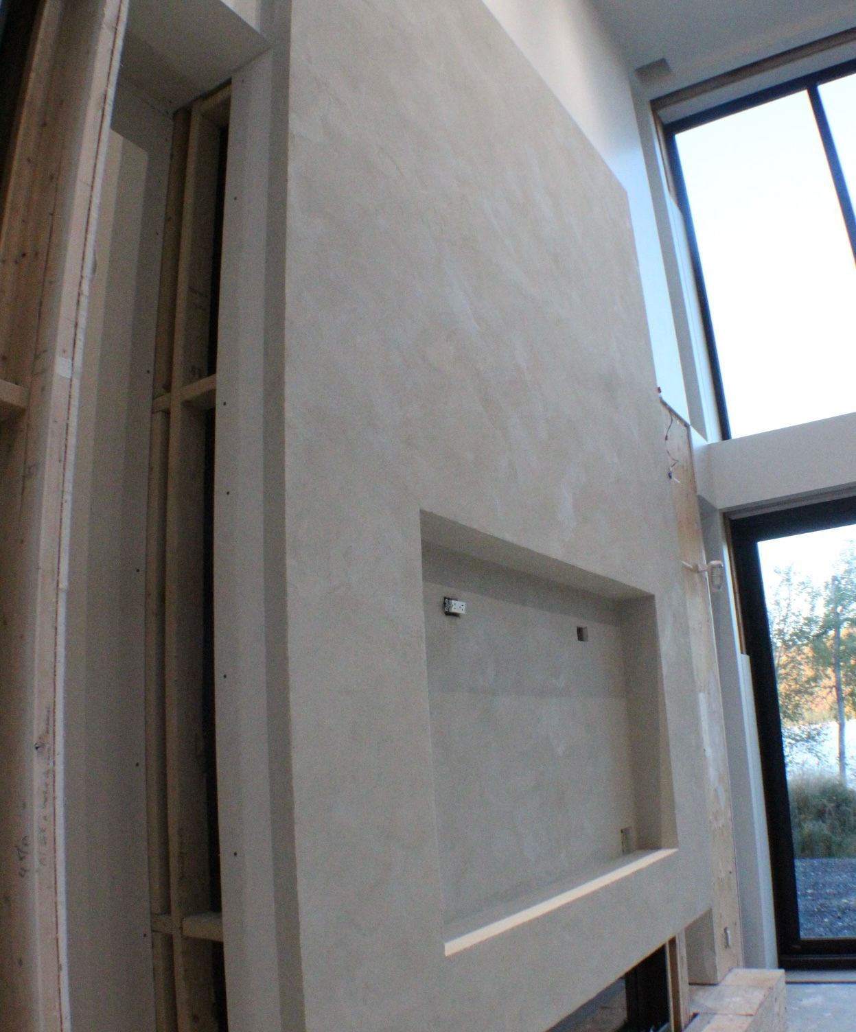 Un mur avec du plâtre texturé de couleur claire, un rectangle en retrait et une ossature en bois adjacente.